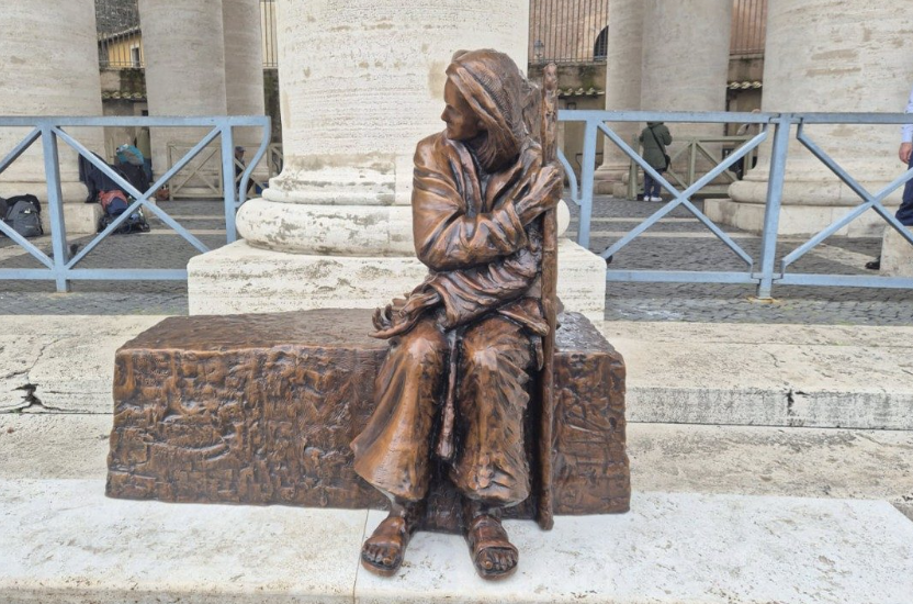 Bronzestatue einer sitzenden Frau vor einer steinernen Säule